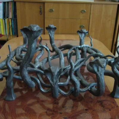 Artystyczne palenisko do kominka o organicznej strukturze wijących się węży i żmij, ciężka konstrukcja stalowa.
