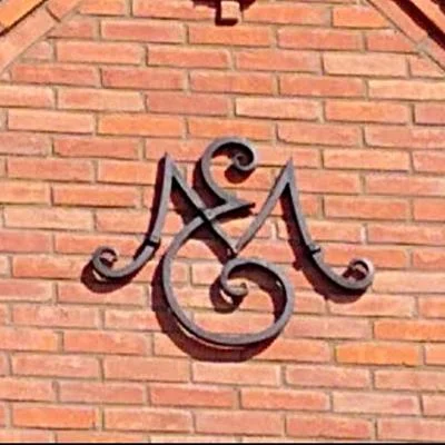 Kuty emblemat architektoniczny wykonany z pełnych prętów stalowych jako ozdobne zwieńczenie budynku stylizowanego na dawną szkołę wiejską.