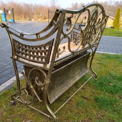 Tył ozdobnej ławki na cmentarz wykonanej metodami kowalstwa artystycznego. Bogata ornamentyka, złota patyna i ręcznie wykonane detale tworzą elegancką przestrzeń pamięci.