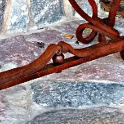 Ozdobny łącznik sekcji artystycznego stojaka rowerowego w stylu rustykalnym z kutymi wolutami, centralną kulą oraz nitowaną konstrukcją inspirowaną historycznym rzemiosłem metalowym.